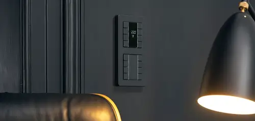 KNX push-button F 50 and KNX room controller F 50 in the AS programme in black, room section with switched-on table people in the foreground.