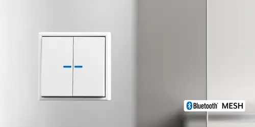 Pulsador de 2 gangs JUNG HOME de la serie LS 990 en blanco, mostrado con una ligera perspectiva y el logotipo Bluetooth® Mesh en la parte inferior derecha