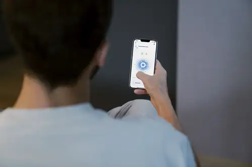 Bauherr von hinten betrachtet, der ein Smartphone mit der JUNG HOME App in der Hand hält. Das Display zeigt die Bewegungsmelder-Ansicht.