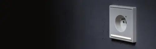 Prise française avec éclairage d'orientation dans le programme LS 990 en blanc alpin, image d'application dans l'obscurité avec éclairage d'orientation lumineux