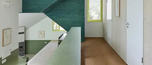 Interieurfoto van een modern huis met groene accentmuur, geel omlijste ramen en witte trapleuningen. Links op de foto is een open haard zichtbaar.