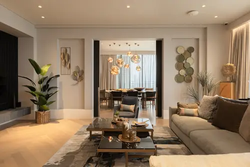 Modern living room in natural colours and materials, dining room with eye-catching ceiling lights in the background.