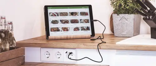Steckdose im Programm LS 990 mit USB-Anschluss in Alpinweiß aus Thermoplast, Ambienteaufnahme in moderner Küche mit Tablet.