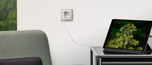 Steckdose mit USB-Anschluss im Programm LS 990 in Edelstahl. Ambienteaufnahme zeigt Ladevorgang eines Tablets.