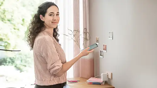 Lächelnde Frau mit gelocktem Haar schaut in die Kamera und hält ein Smartphone mit der JUNG HOME App in der Hand.