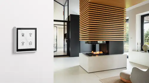 LS TOUCH im Programm LS 990 in Alpinweiß. Ambienteaufnahme mit einem stylischen Wohnzimmer und Kamin in der Mitte des Raums im Hintergrund.