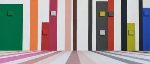 Verschiedene Schalter im Programm Les Couleurs® Le Corbusier in unterschiedlichen Farben, frontal auf einer bunten Wand aus Streifen.