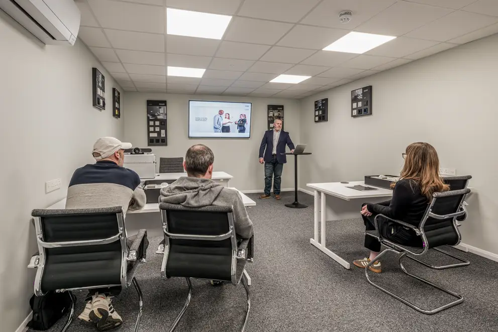 Trainees receive instruction in the training room of the JUNG training centre in London. The trainee standing at a lectern is at the front at the back of the room and the three trainees are sitting with their backs to the photographer.