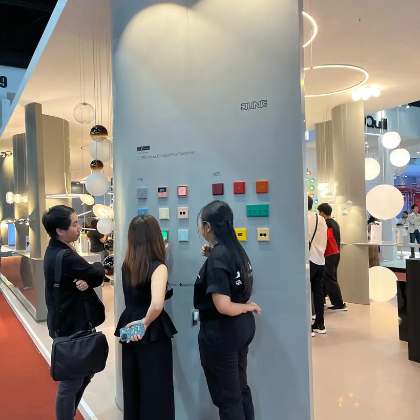 Three people look at a JUNG display board on the trade fair stand at the Architect Expo.