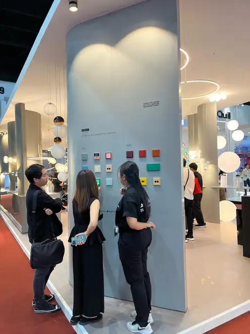 Three people look at a JUNG display board on the trade fair stand at the Architect Expo.