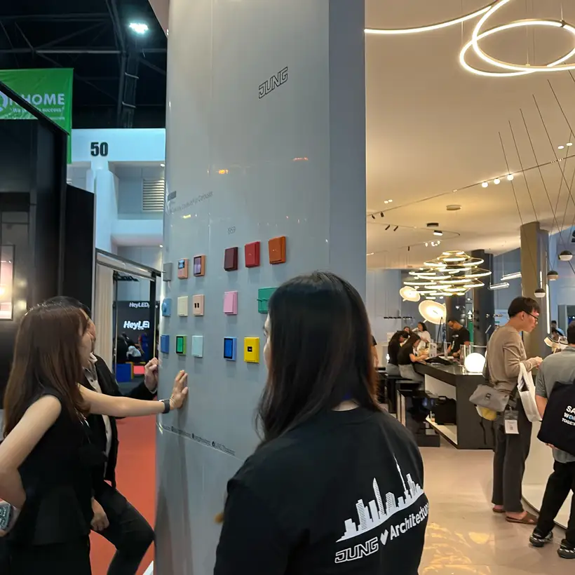 Three people look at a JUNG display board on the trade fair stand at the Architect Expo 2024.