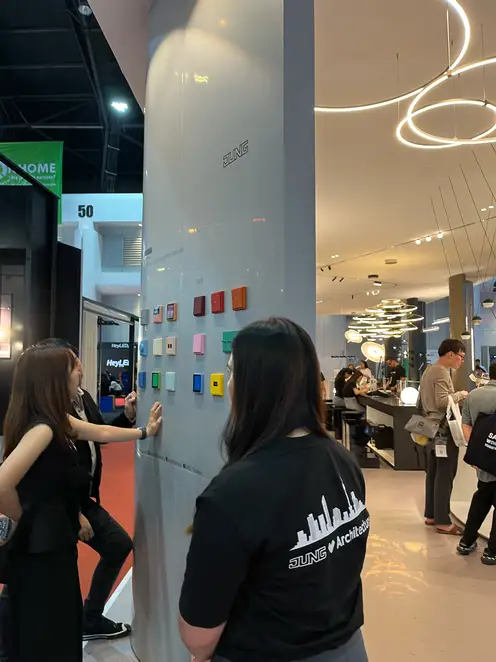 Three people look at a JUNG display board on the trade fair stand at the Architect Expo 2024.
