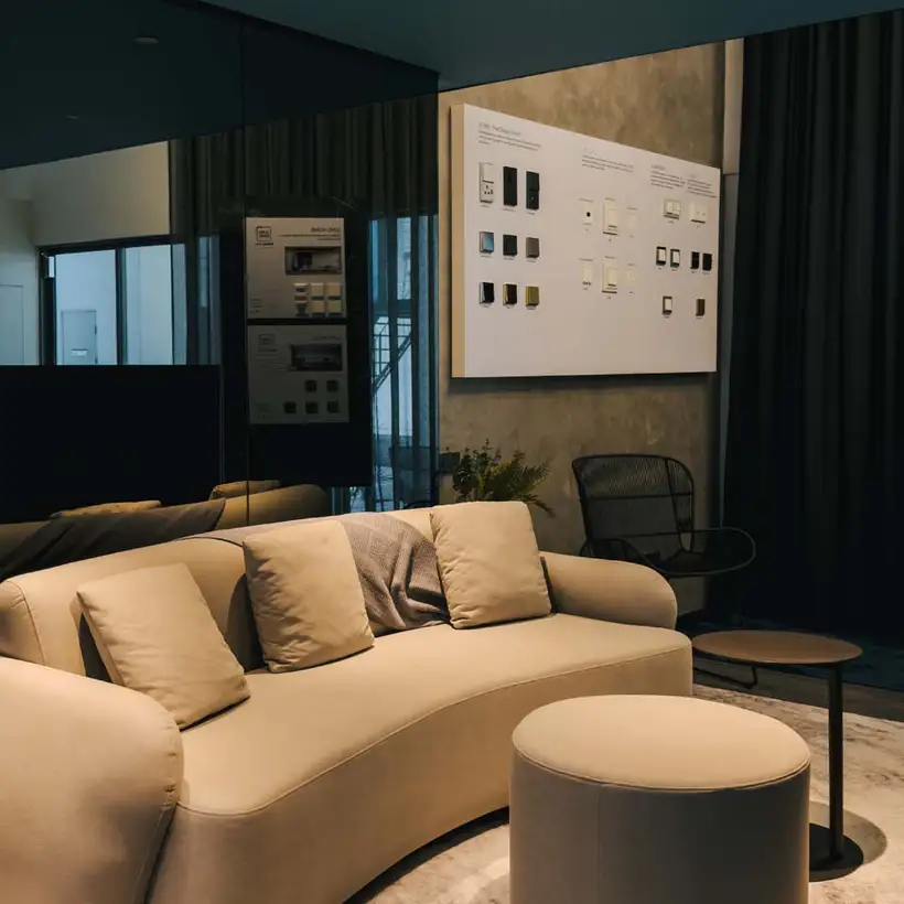 Brandstore Kuala Lumpur, Sitzecke mit beigefarbener Couch vor schwarzer spiegelnder Wand neben Präsentationsdisplay