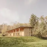 Das Walderlebniszentrums, Leupoldishain von außen. Es steht auf einer weiten Wiese mit vielen Bäumen.