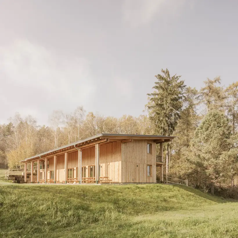 Das Walderlebniszentrums, Leupoldishain von außen. Es steht auf einer weiten Wiese mit vielen Bäumen.