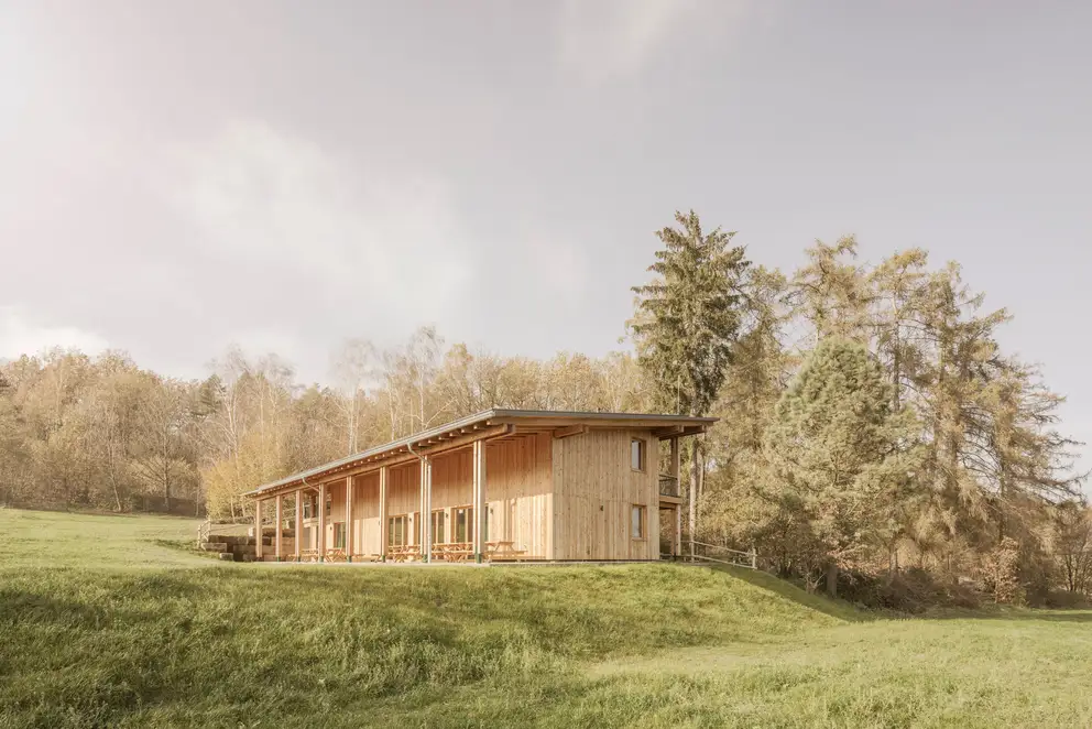 Das Walderlebniszentrums, Leupoldishain von außen. Es steht auf einer weiten Wiese mit vielen Bäumen.