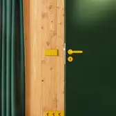 Zwischen einer grünen Tür und einem grünen Vorhang befindet sich eine Holzwand. Auf der Wand sind Schalter und Steckdosen in LS 990 Messing Klassik montiert. 