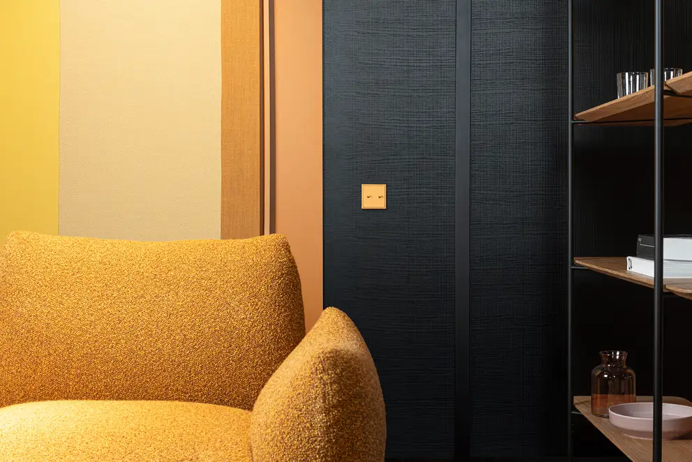 Lichtschalter im Programm LS 1912 in Les Couleurs® Le Corbusier in leichter Perspektive. Detailaufnahme mit einem Sessel und Bücherregal im Anschnitt.