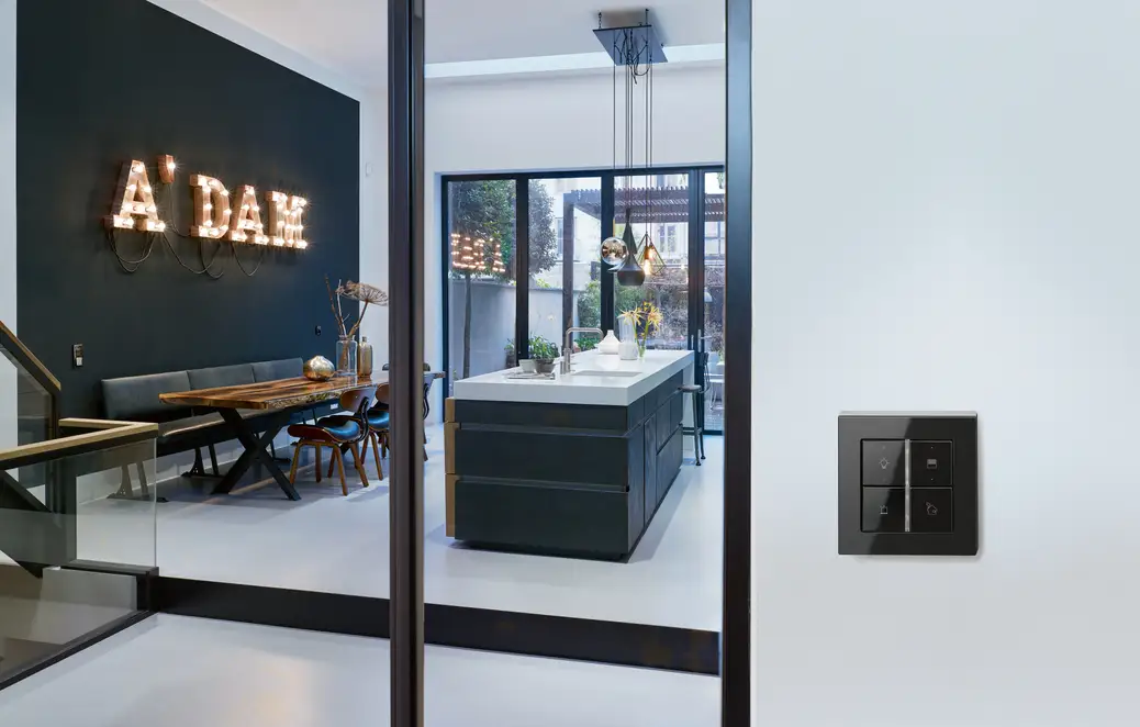 KNX F 40 Taster im Programm A550 in schwarz aus bruchsicherem Thermoplast, Ambienteaufnahme mit einer A'DAM Leuchtschrift im Hintergrund.