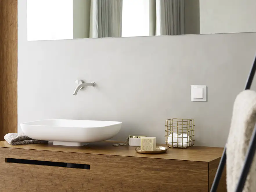 Taster im Programm A Creation aus Glas in Alpinweiß, leicht perspektivisch aufgenommen, über einem Massivholz-Waschtisch, in einem hellen Badezimmer.