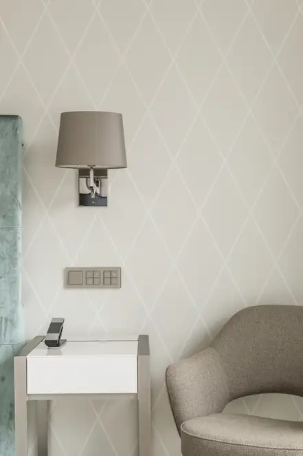 KNX Taster F 40 und SCHUKO® Steckdosen im Programm A Creation aus Glas in Champagner. Ambienteaufnahme im Raumausschnitt, frontal fotografiert, über einem Nachtisch in einem der Hotelzimmer des The Fontenay, Hamburg.