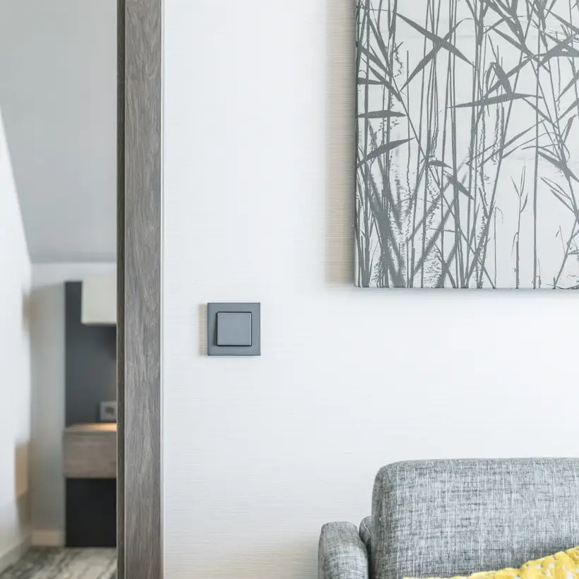 Taster im Programm A Creation aus Kunststoff, frontal aufgenommen, im Raumausschnitt eines Hotelzimmers des Parkhotel Kranz Siegburg. Rechtsseitig befindet sich im Anschnitt ein grau bezogener Sessel, über welchem ein großformatiges Bild hängt.