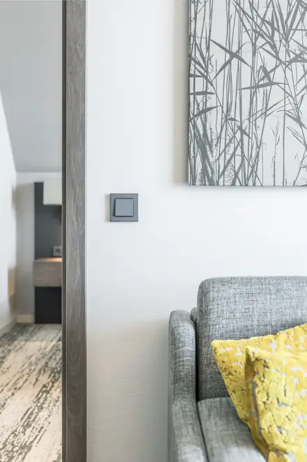 Taster im Programm A Creation aus Kunststoff, frontal aufgenommen, im Raumausschnitt eines Hotelzimmers des Parkhotel Kranz Siegburg. Rechtsseitig befindet sich im Anschnitt ein grau bezogener Sessel, über welchem ein großformatiges Bild hängt.