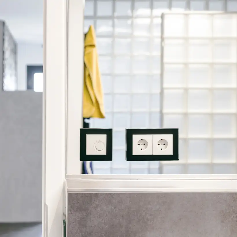 eNet Smart Home Produkte im Programm LS PLUS in Schwarz, aufgenommen in einem hellen Badezimmer vor Spiegelfläche.