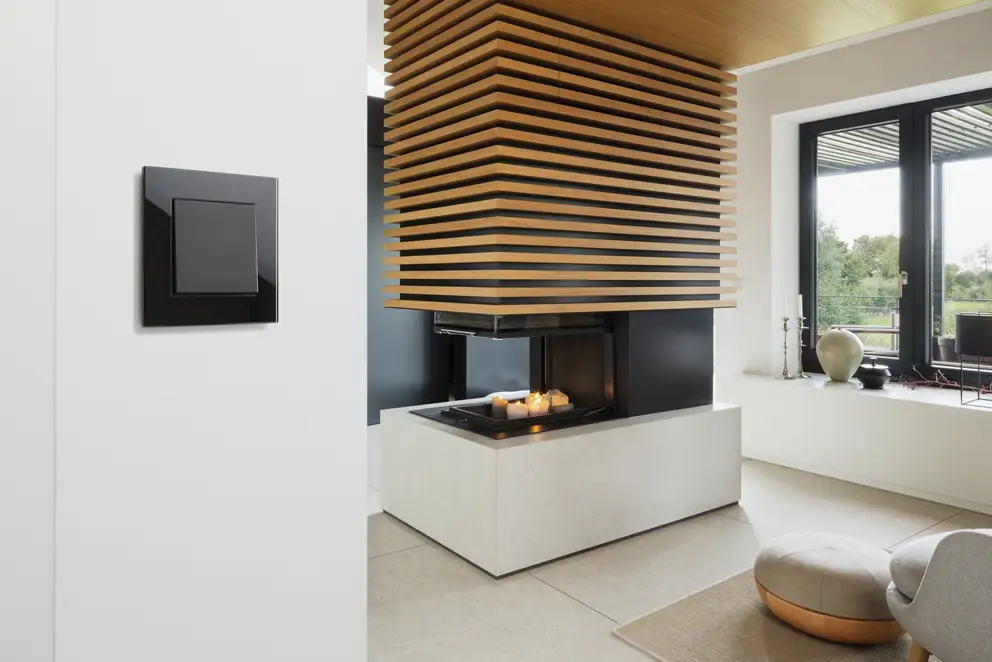 Taster im Programm LS PLUS in Schwarz, aufgenommen vor heller Sitzecke mit Kamin.