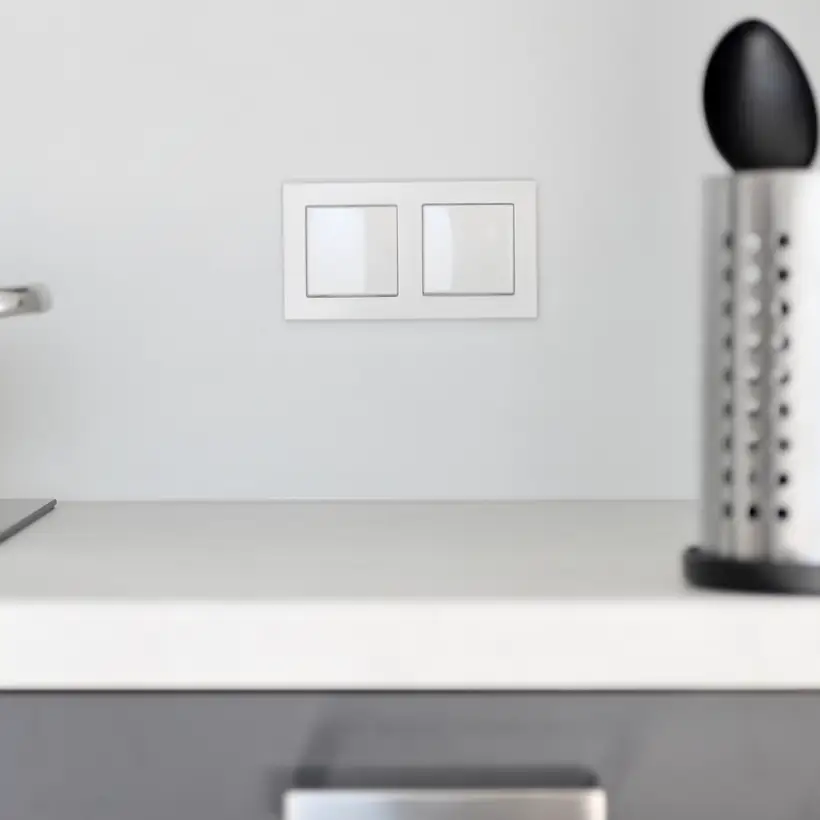 Taster im Programm A Creation aus Kunststoff in Alpinweiß, frontal fotografiert mit geringer Tiefenschärfe, so dass die im Ausschnitt gezeigte Küchenzeile und die darauf stehenden Töpfe und Utensilien eine Unschärfe haben.