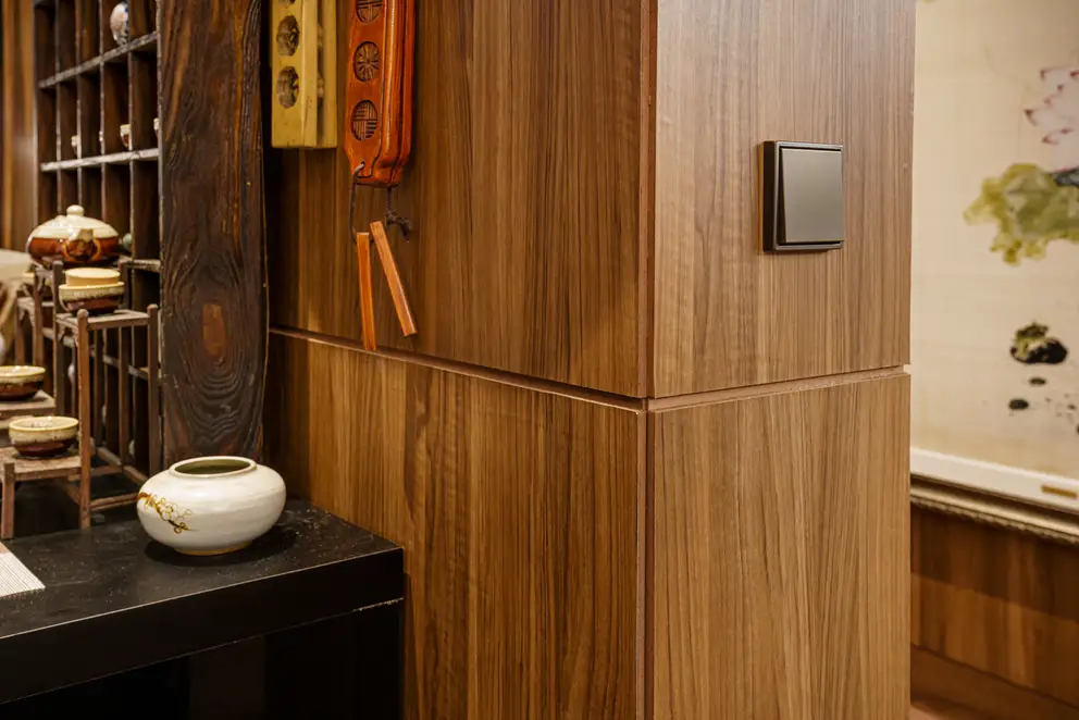 Taster im Programm LS 990 in Messing Antik, aufgenommen in Perspektive, vor einem mit Holz verkleidetem Durchgang. Linksseitig befinden sich asiatische Teekannen weiter hinten im Raum.