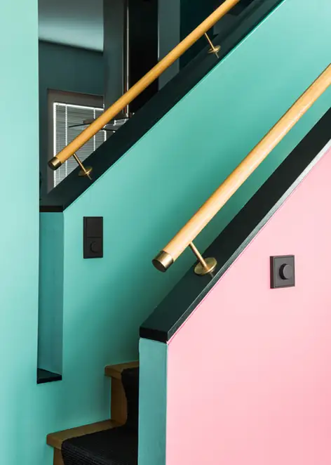 Der LS 990 Drehdimmer in Les Couleurs® Le Corbusier universellem Farbsystem, fotografiert in leichter Perspektive, an einem Pink gestrichenen Treppenaufgang mit schwarzen Akzenten und Holzhandlauf. 