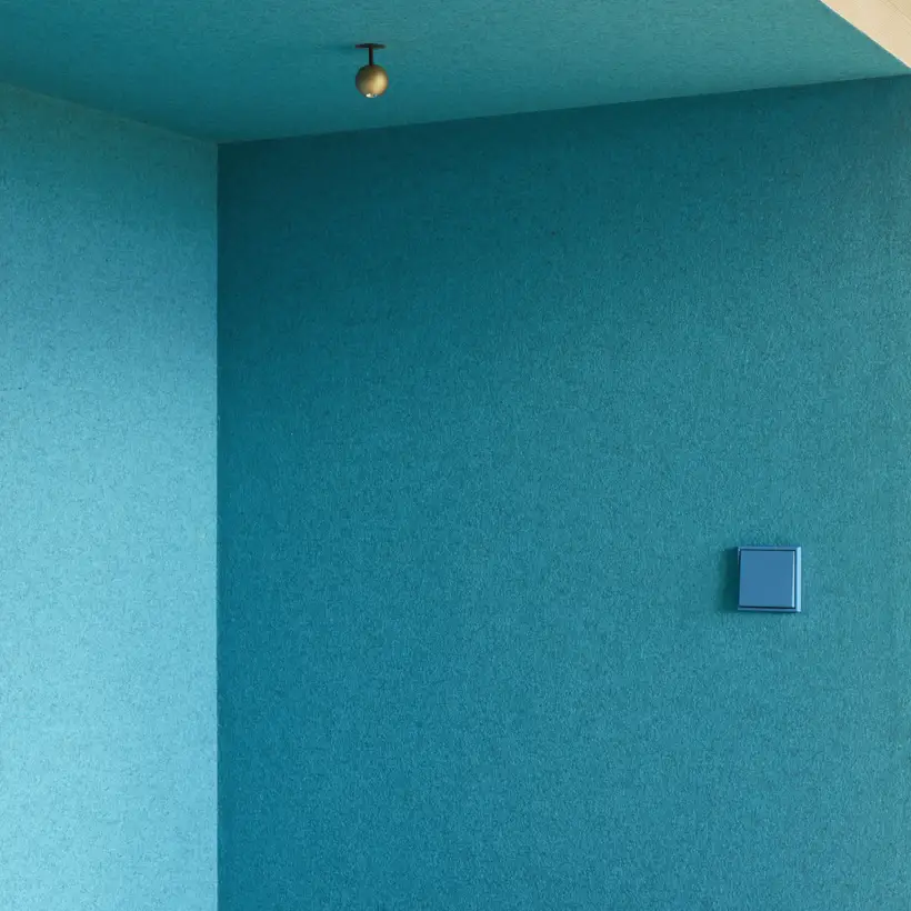 Ambienteaufnahme des LS 990 Taster in Les Couleurs® Le Corbusier in 32030 bleu ceruleen 31, fotografiert im Raumausschnitt auf blauer Wand im Ferienhaus Rotenberg.