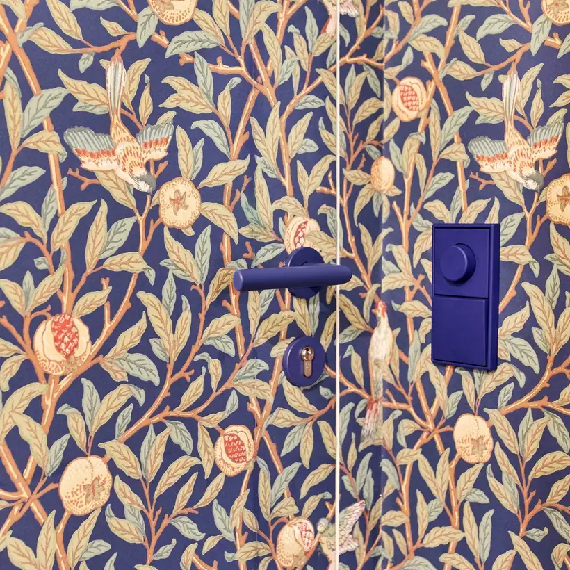 LS 990 Drehdimmer und Taster in Les Couleurs® Le Corbusier universellem Farbsystem, Ambienteaufnahme „Wohnen mit Morris“ Apartment in Stuttgart. Taster und Drehdimmer sind farblich passend zu dem Blau der floralen Tapete gewählt. Fotografiert in leichter 