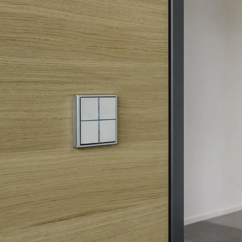 KNX F 40 Taster aus Edelstahl, fotografiert in leichter Perspektive auf einem Holzhintergrund.