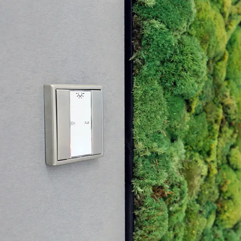 Taster F 50 für KNX aus Edelstahl, fotografiert in leichter Perspektive, vor einer grauen Wand. Im Ausschnitt sieht man ein Moosildb