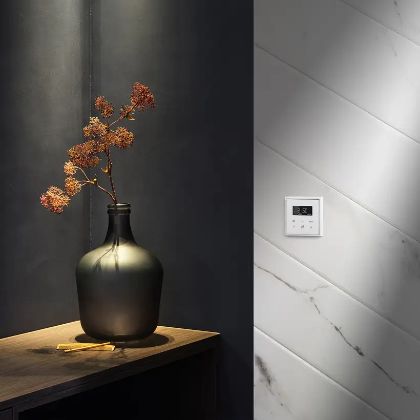 Raumthermostat im Programm LS 990 in Alpinweiß. Ambienteaufnahme vor einer stilvollen Marmor-Wand, mit moderner Vase. 