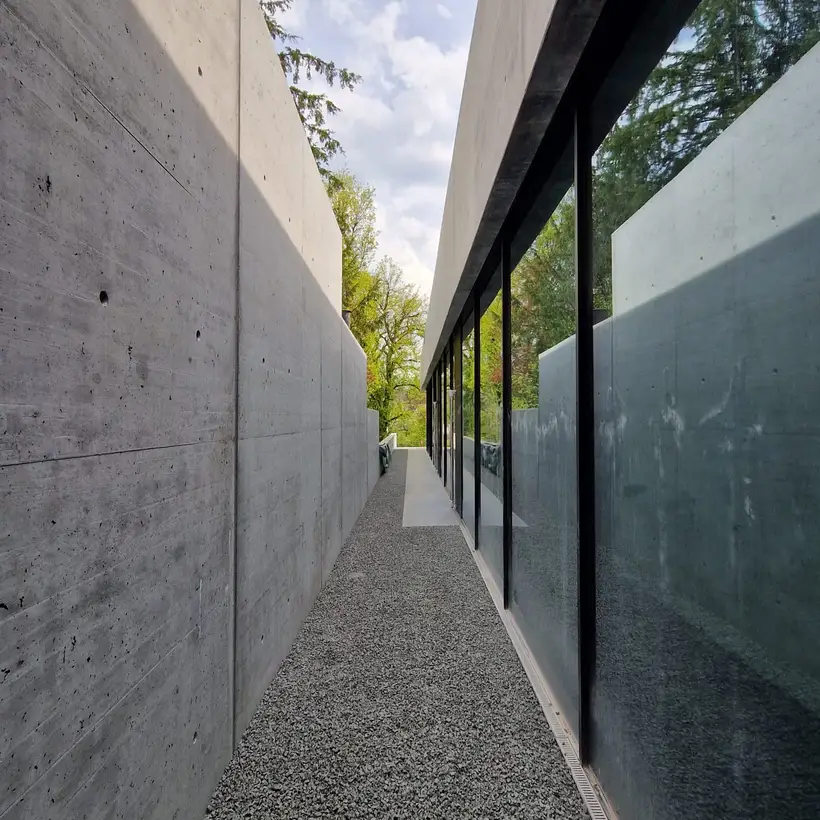 Seitenansicht des Pavillons der Gründervilla in Schalksmühle. In einer langen Flucht entlang einer Glasfront fotografiert, so dass sich rechtsseitig nur Fenster und linksseitig eine lange Betonaußenwand befindet.