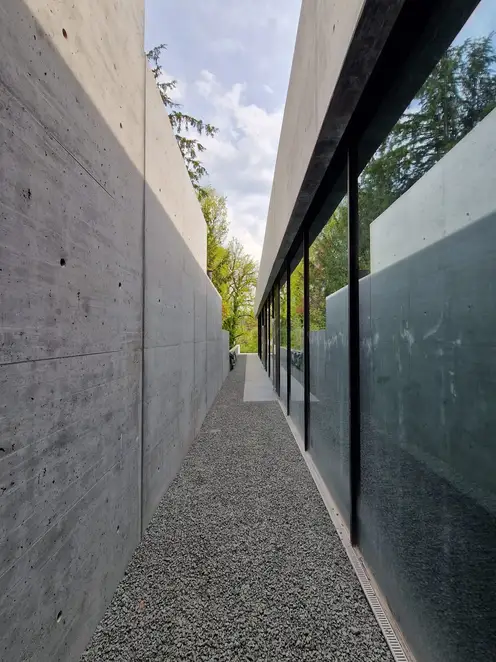 Seitenansicht des Pavillons der Gründervilla in Schalksmühle. In einer langen Flucht entlang einer Glasfront fotografiert, so dass sich rechtsseitig nur Fenster und linksseitig eine lange Betonaußenwand befindet.